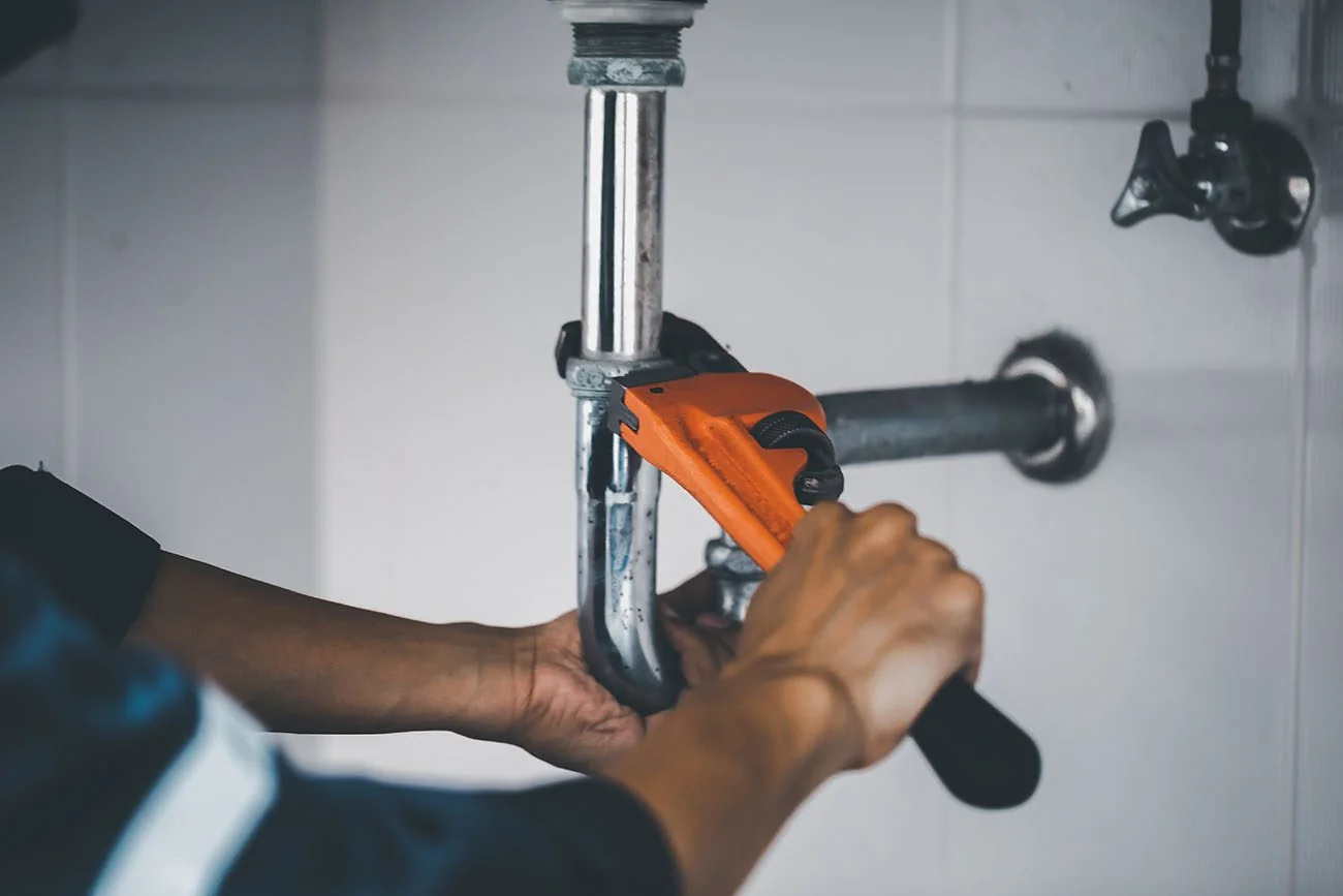 Hands using a pipe wrench on a drain connection beneath a sink